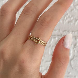 May include: A set of three gold rings, one with a knot design and two with a chain design.