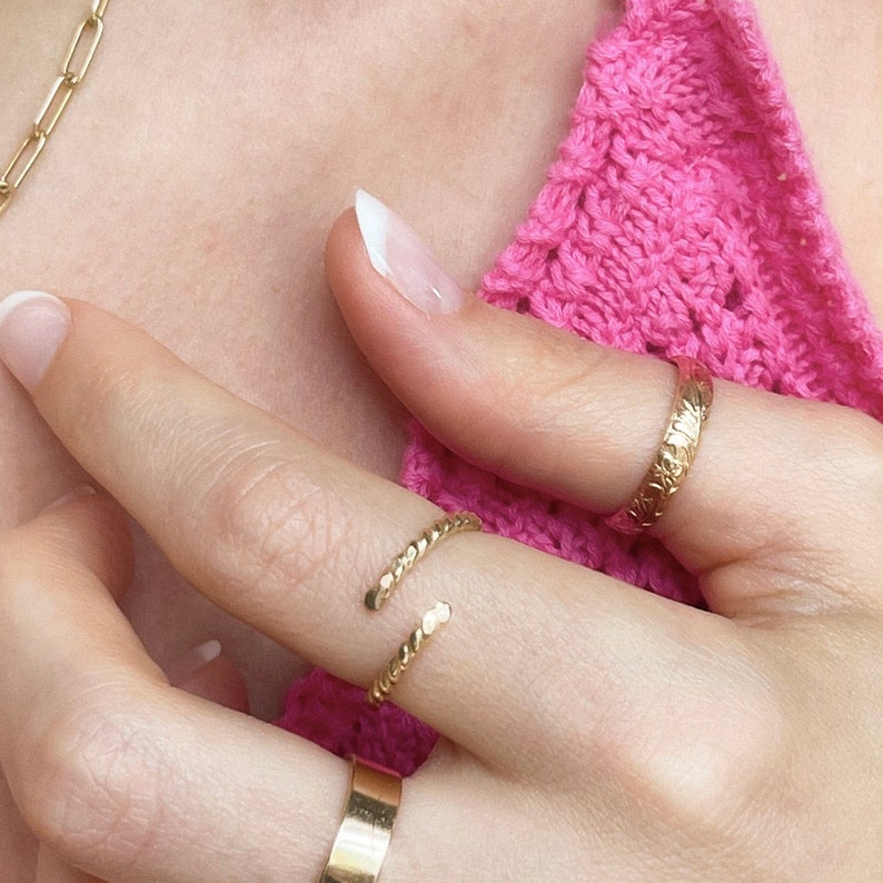 May include: Two gold rings on a finger. One ring is a simple band, the other is a twisted band.