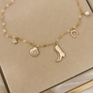 May include: A gold chain necklace with five charms: a star, a seashell, a boot, a horseshoe, and a pearl.