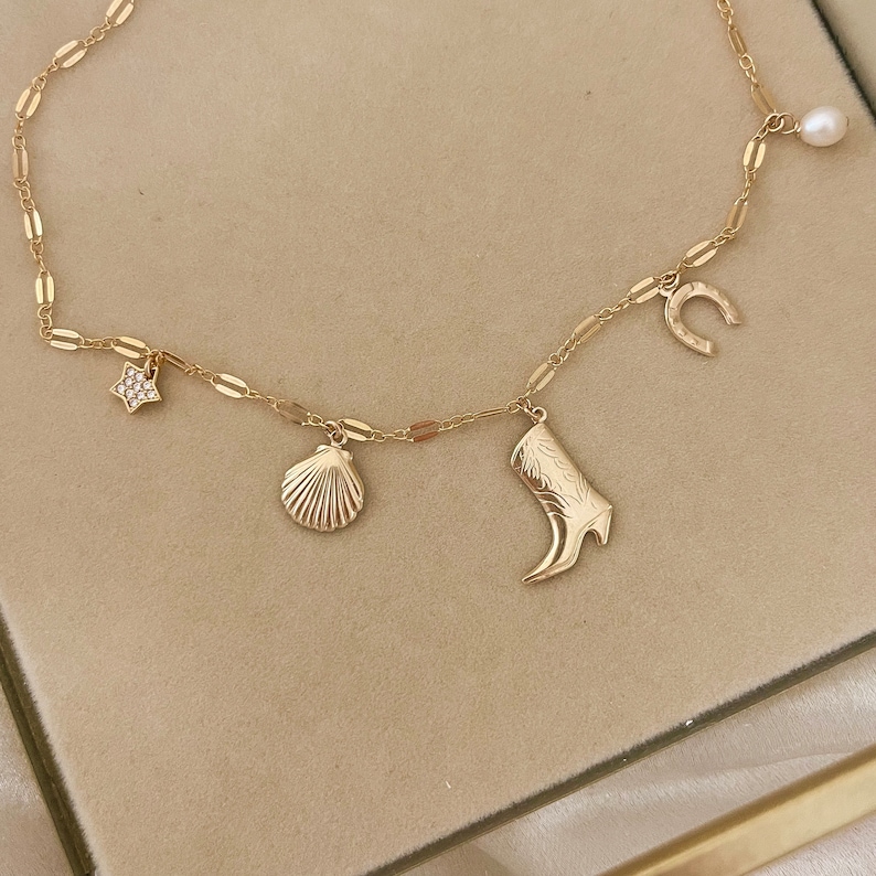 May include: A gold chain necklace with five charms: a star, a seashell, a boot, a horseshoe, and a pearl.