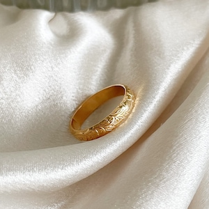 May include: A gold band ring with an intricate floral design. The ring is smooth and polished.