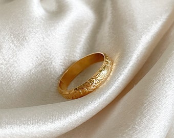 May include: A gold band ring with an intricate floral design. The ring is smooth and polished.