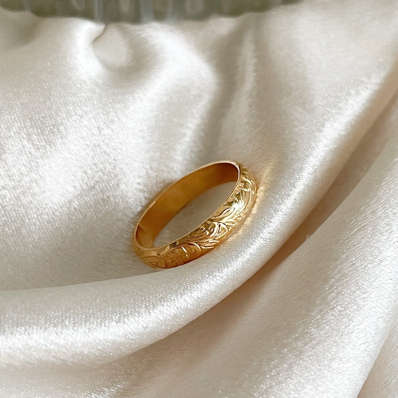 May include: A gold band ring with an intricate floral design. The ring is smooth and polished.