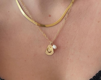 Puede incluir: Un collar de cadena de oro con un colgante de oro en forma de sombrero de vaquero y un pequeño dije de perla.