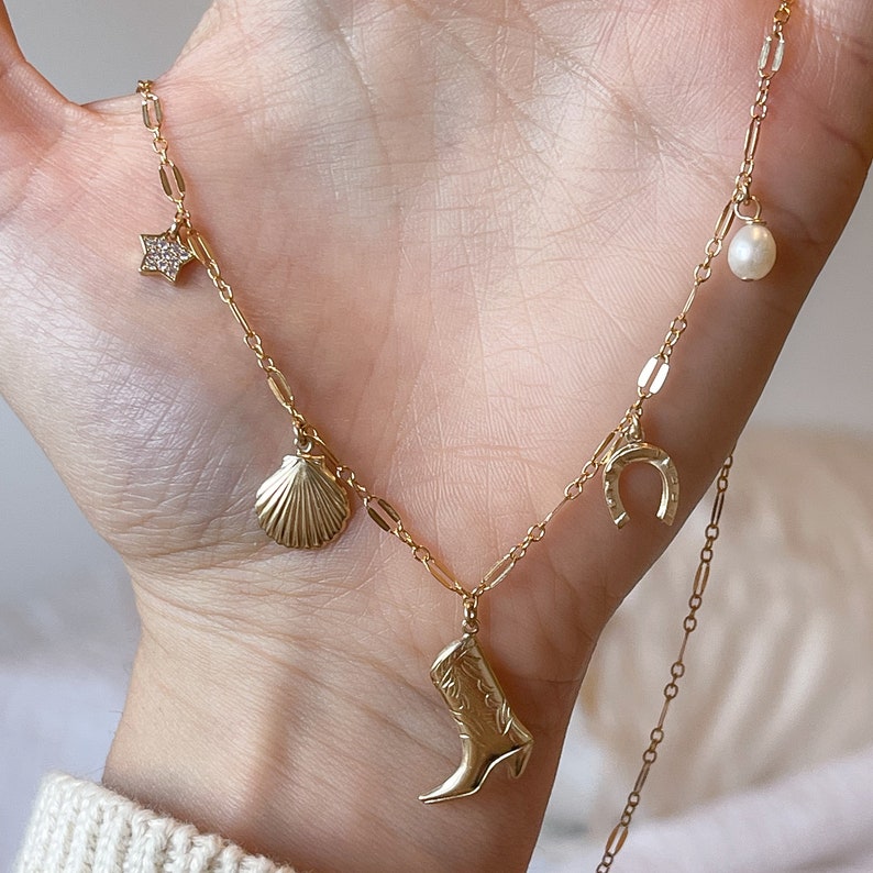 May include: A gold chain necklace with a variety of charms, including a seashell, a horseshoe, a star, a boot, and a pearl.