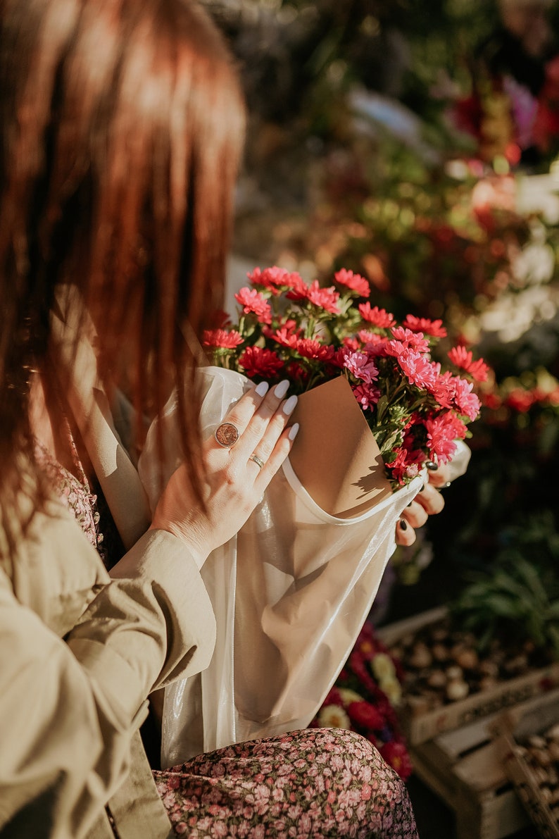 May include: A person holding a bouquet of pink and red flowers wrapped in a white paper bag. The flowers are in a clear plastic bag.