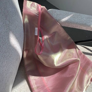 Op de afbeelding: Een roze, iriserende mesh-tas met een roze satijnen band en een wit label met de tekst "LABEL" erop.