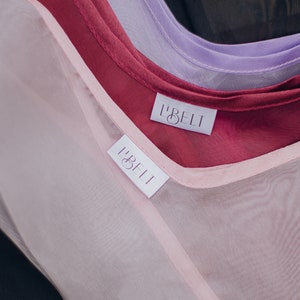 May include: Three sheer fabric scarves in pink, burgundy, and lavender with white labels that read "L'BELT" on each.