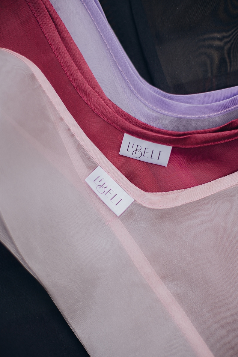 May include: Three sheer fabric scarves in pink, burgundy, and lavender with white labels that read "L'BELT" on each.