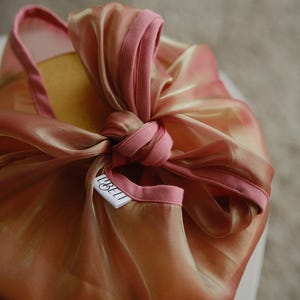 May include: A pink and gold fabric gift wrap with a white tag that says "LIBELLI" on it.