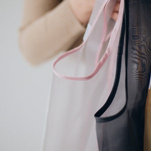 May include: Two sheer fabric bags with pink and black trim. The bags are held by a hand.
