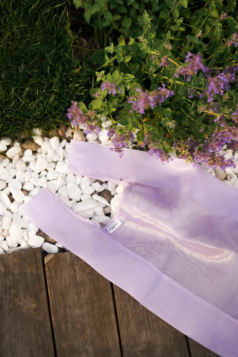May include: A light purple reusable shopping bag made of mesh fabric with the word "LILLA" printed on the front.