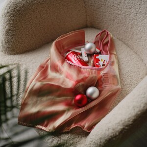 May include: A pink mesh tote bag filled with a can of Coca-Cola, red and silver baubles, and other small items. The bag is sitting in a fluffy white chair.