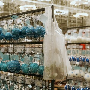 May include: A display of Christmas ornaments in a store. The ornaments are various shades of blue and white, with glitter and striped designs. A clear plastic bag hangs on the display, filled with more ornaments and greenery.