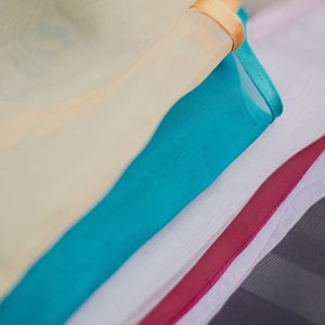 May include: A stack of fabric scraps in various colors, including cream, turquoise, white, and burgundy. The top scrap has a gold trim.