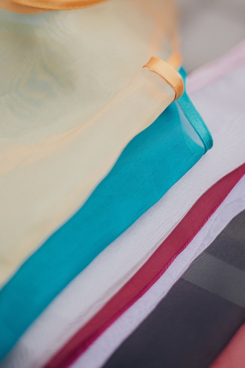 May include: A stack of fabric scraps in various colors, including cream, turquoise, white, and burgundy. The top scrap has a gold trim.
