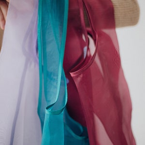 May include: Four sheer fabric scarves in shades of lavender, teal, and burgundy.