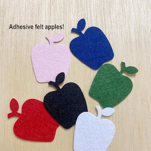 May include: Six felt apple shapes in various colors: pink, blue, green, black, red, and white. The apples are cut out and have a stem and leaf. The text "Adhesive felt apples!" is in the top left corner of the image.