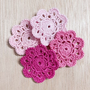 May include: Four crocheted doilies in shades of pink and fuchsia, with intricate floral designs. The doilies are arranged in a cluster on a light wood surface.