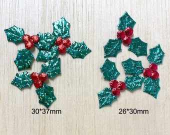 May include: Two sets of green holly leaf embellishments with red berries. The larger set measures 30 by 37 mm and the smaller set measures 26 by 30 mm.