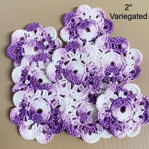 May include: A collection of 10 crocheted purple and white flowers, each measuring 2 inches in diameter. The flowers are variegated, meaning they have a gradient of color from purple to white.