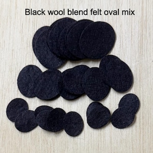 May include: A collection of black wool blend felt oval shapes in various sizes. The felt pieces are arranged on a light wood-grain surface. The text "Black wool blend felt oval mix" is at the top of the image.