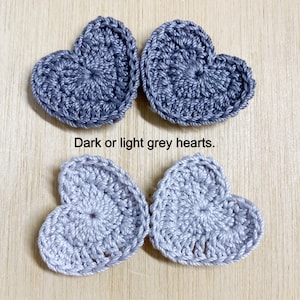 May include: Four crocheted heart shapes in shades of gray. Two are a darker gray, and two are a lighter gray. The text "Dark or light grey hearts" is below the hearts.