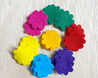 May include: A set of ten felt flower shapes in various colors, including pink, green, yellow, red, and purple. The flowers are arranged in a circle on a light wood surface.