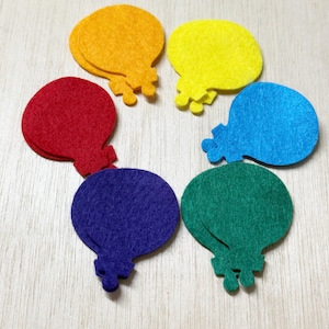 May include: Six colorful felt balloon shapes in red, orange, yellow, blue, green, and purple are arranged in a circle. Each balloon has a small, detailed base. The felt material has a soft, textured appearance.