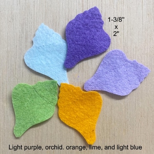 May include: Five felt seashell cutouts in purple, light blue, light purple, lime green, and orange. Each piece measures 1-3/8 inches by 2 inches. The shapes feature stitched detailing on the surface, arranged in a cluster on a flat surface.