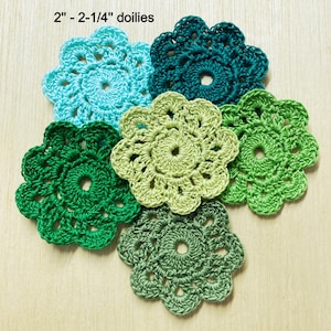May include: Five crocheted doilies in shades of green and blue. The doilies are 2 - 2-1/4 inches in diameter.