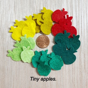May include: A collection of felt apple shapes in red, green, and yellow. The apples are arranged in a circle around a US penny.