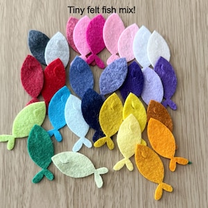 May include: A collection of colorful felt fish in various shades, including pink, blue, yellow, and orange. The fish have a simple, stylized design with a tail fin. The text "Tiny felt fish mix!" is at the top.