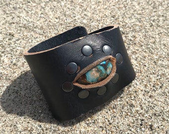 May include: Black leather cuff bracelet with a turquoise stone inlay and silver studs.