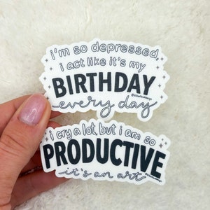 May include: Two white stickers with black text. The top sticker reads "i'm so depressed, i act like it's my BIRTHDAY every day". The bottom sticker reads "i cry a lot, but i am so PRODUCTIVE it's an art".
