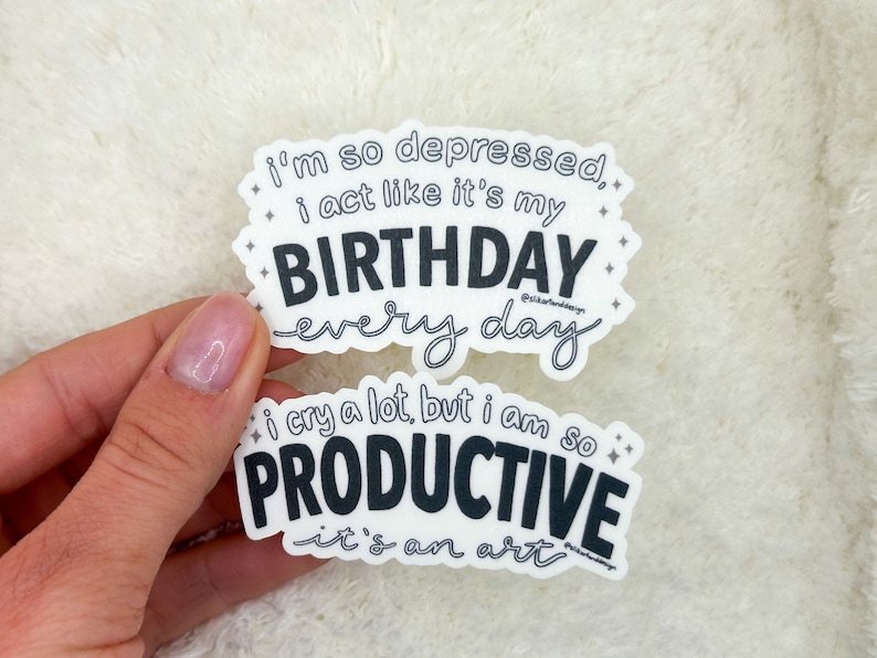 May include: Two white stickers with black text. The top sticker reads "i'm so depressed, i act like it's my BIRTHDAY every day". The bottom sticker reads "i cry a lot, but i am so PRODUCTIVE it's an art".