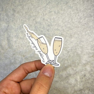 May include: A white sticker with a hand-drawn illustration of two champagne glasses with champagne pouring out of one of the glasses. The text "champagne problems" is written on the sticker.