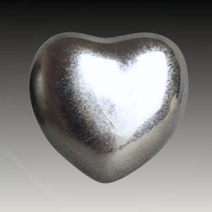 Puede incluir: Una caja de recuerdo en forma de corazón de plata con una superficie texturizada.