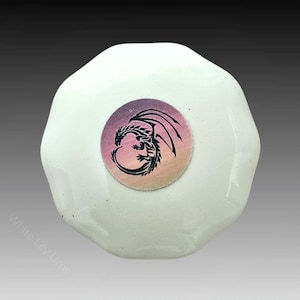 Puede incluir: Urna de cremación de cerámica blanca con un diseño redondo en degradado rosa y morado que presenta una silueta negra de un dragón.