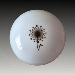May include: White ceramic lid with a gold dandelion design.
