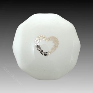 Puede incluir: Caja de cerámica blanca con un diseño de corazón decorativo en plata y oro.
