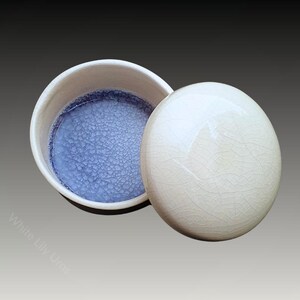 Puede incluir: Un tarro de cerámica blanco con tapa, el interior está cubierto con un esmalte craquelado azul. La tapa está cubierta con un esmalte craquelado blanco.