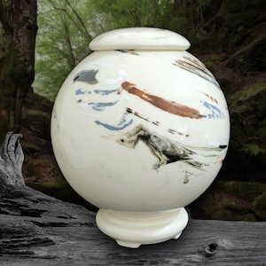 May include: White ceramic urn with a lid, featuring abstract brushstrokes in shades of blue, brown, and gray. The urn has a round body and a small base.