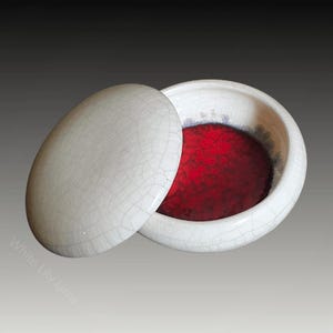 May include: A white ceramic lidded bowl with a red interior. The bowl has a crackled glaze finish.