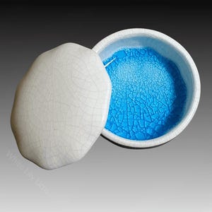 Puede incluir: Caja de cerámica blanca para pequeños objetos con un interior de esmalte azul craquelado. La tapa es octogonal y tiene un esmalte blanco craquelado.