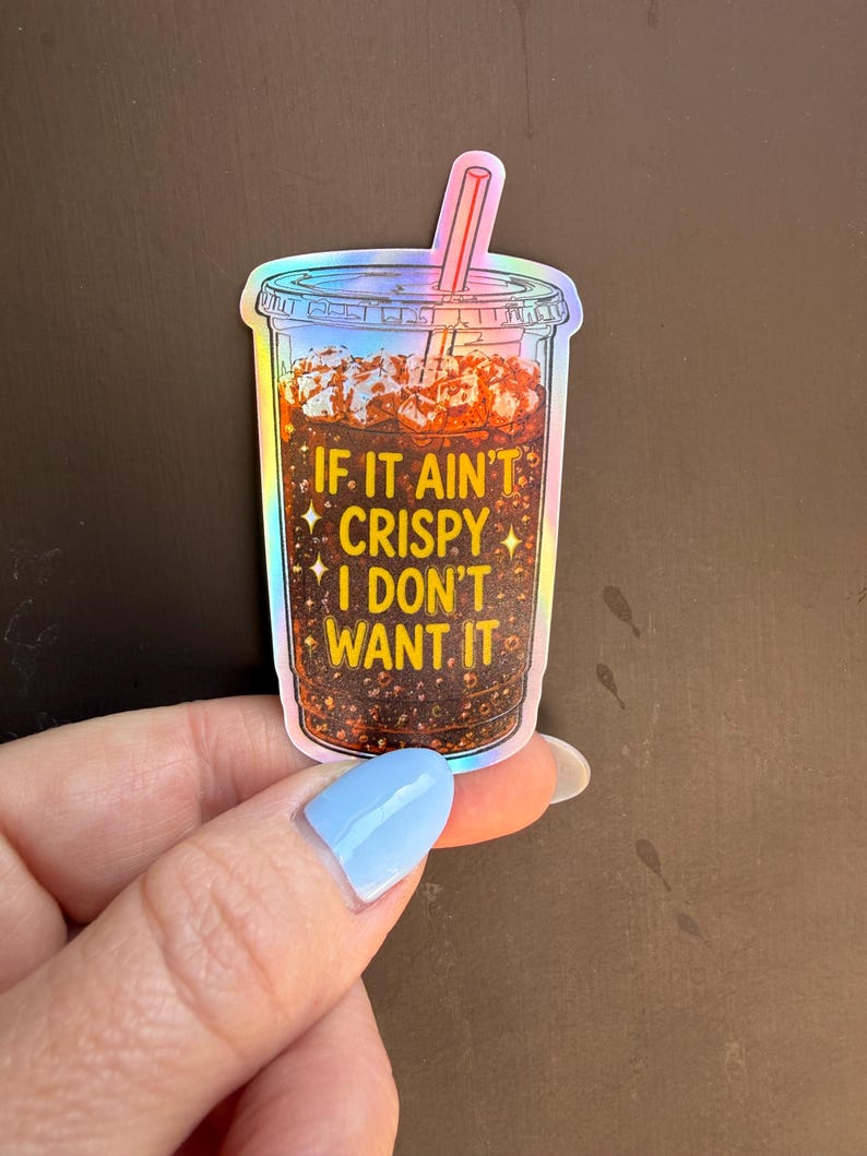 May include: A holographic sticker shaped like a clear plastic cup filled with a dark brown carbonated beverage, ice cubes, and a pink straw. The text IF IT AIN'T CRISPY I DON'T WANT IT is printed in yellow letters on the front of the cup.