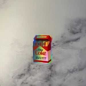 K&ouml;nnte beinhalten: Ein Aufkleber, der einer Diet Coke-Zigarettenschachtel &auml;hnelt. Die Schachtel ist rot und tr&auml;gt das Diet Coke-Logo und den Text "JUST A LITTLE SOMETHING TO TAKE THE EDGE OFF". Auf der Oberseite der Packung steht "FRIDGE CIGS".