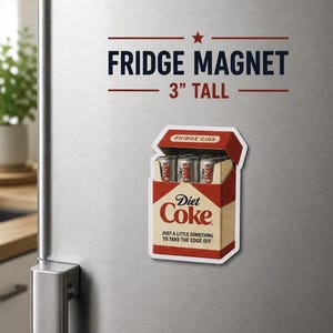 K&ouml;nnte beinhalten: Ein K&uuml;hlschrankmagnet mit dem Text "FRIDGE MAGNET" und "3" TALL". Der Magnet zeigt eine Schachtel mit "Diet Coke" Dosen mit der Aufschrift "FRIDGE CIGS". Der Text "JUST A LITTLE SOMETHING TO TAKE THE EDGE OFF" ist ebenfalls vorhanden. Die H&ouml;he betr&auml;gt ca. 7,6 cm.