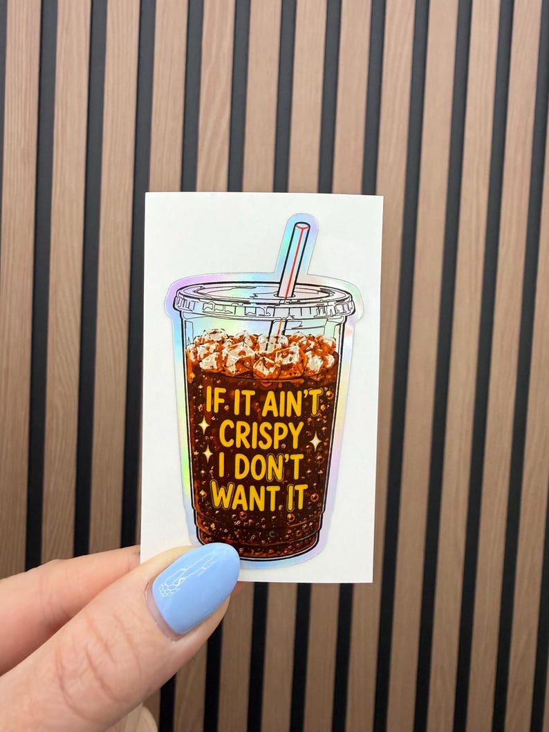May include: A holographic sticker featuring a clear plastic cup filled with dark brown iced coffee and ice cubes. A straw sticks out of the lid. The text IF IT AIN'T CRISPY I DON'T WANT IT is printed in yellow on the front of the cup.