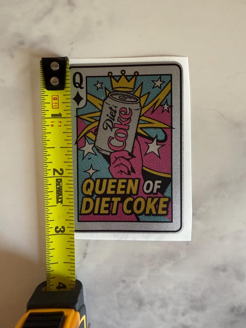 May include: A sticker featuring a playing card design with a Diet Coke can held by a hand. The text "Queen of Diet Coke" is displayed in a retro font. The sticker measures approximately 3 inches in height.
